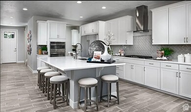 Kitchen with backsplash, wood tiled floors, an island with sink, white cabinetry, and recessed lighting