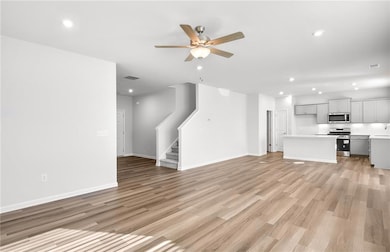 Unfurnished living room featuring a ceiling fan, light wood-style flooring, stairway, recessed lighting, and baseboards