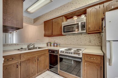 Kitchen with appliances with stainless steel finishes, a sink, light tile patterned flooring, light countertops, and wallpapered walls