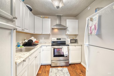 Kitchen with freestanding refrigerator, wall chimney exhaust hood, electric stove, wood finished floors, and a textured ceiling