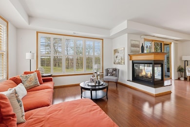 High tray ceilings, 3-sided gas fireplace, luxury wood plank flooring, and elegant white shutters overlooking the path to the lake.