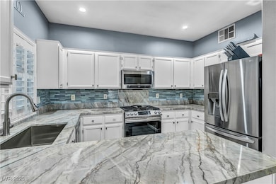 Kitchen featuring white cabinets, stainless steel appliances, quartz counters, tiled backsplash, and recessed lighting