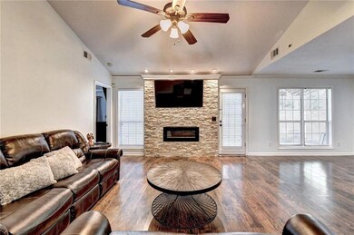 Living room featuring vaulted ceiling, a ceiling fan, a fireplace, wood finished floors, and ornamental molding