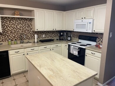 Kitchen featuring range with electric cooktop, a center island, a sink, white microwave, and black dishwasher