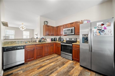 Kitchen with stainless steel appliances, a chandelier, hardwood / wood-style flooring, light stone countertops, and brown cabinetry