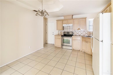 Kitchen with light brown cabinets, backsplash, white fridge, a chandelier, and stainless steel range with electric stovetop