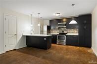 Kitchen with stainless steel appliances, a peninsula, light countertops, dark cabinetry, and hanging light fixtures