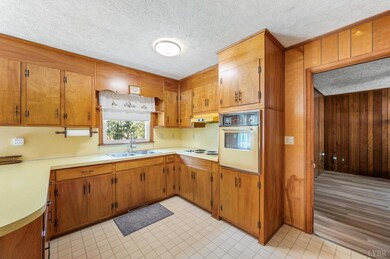 Kitchen with wood cabinetry, yellow backsplash, wall oven, and tile flooring. - 5292 Java Rd, Java, VA 24565