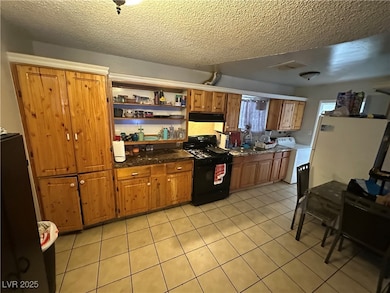 Kitchen featuring black range with gas stovetop, light tile patterned floors, washer / clothes dryer, a textured ceiling, and open shelves