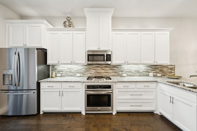 Kitchen with stainless steel appliances, white cabinetry, tasteful backsplash, and light stone countertops