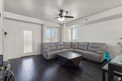 Living area featuring dark wood-type flooring, a ceiling fan, and a textured ceiling