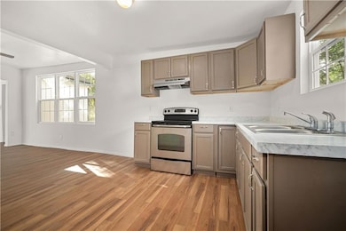 Kitchen with stainless steel electric range, light countertops, light wood-style flooring, and under cabinet range hood