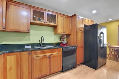 Kitchen featuring black appliances, light wood finished floors, dark stone counters, glass insert cabinets, and brown cabinets