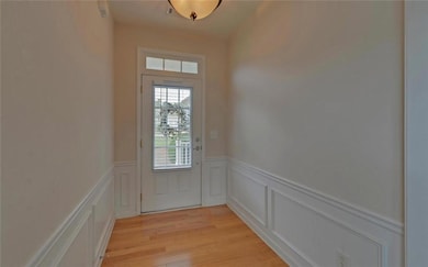 Doorway to outside featuring a wainscoted wall, light wood-type flooring, and a decorative wall