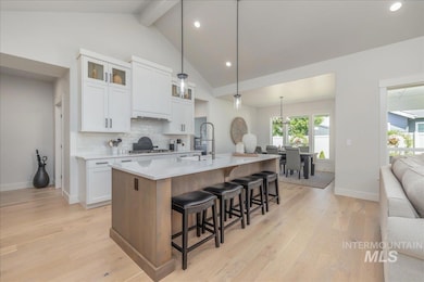 Kitchen featuring beam ceiling, a kitchen breakfast bar, light wood-type flooring, backsplash, and white cabinets