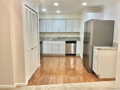 Kitchen with appliances with stainless steel finishes, white cabinetry, crown molding, light wood finished floors, and light stone counters