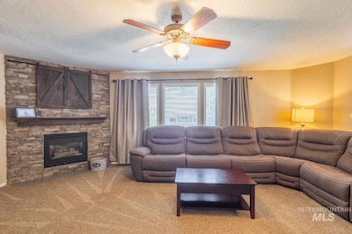 Living area featuring light carpet, a textured ceiling, ceiling fan, and a stone fireplace