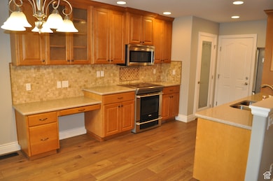 Kitchen featuring appliances with stainless steel finishes, brown cabinetry, glass insert cabinets, decorative backsplash, and light wood-style floors