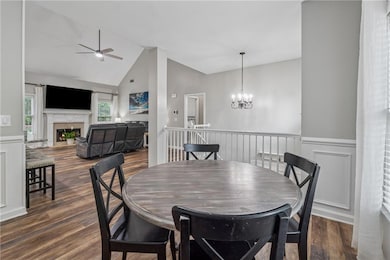 Dining room with a wainscoted wall, a fireplace, ceiling fan, dark wood finished floors, and a chandelier