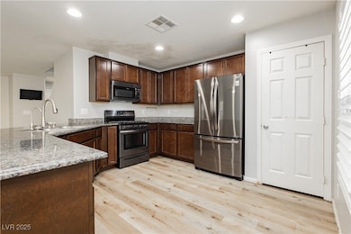 Kitchen featuring light stone counters, stainless steel appliances, light wood finished floors, recessed lighting, and dark brown cabinetry