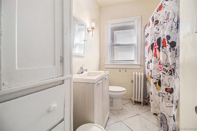 Full bathroom featuring vanity, radiator, light marble finish floors, and a shower with shower curtain