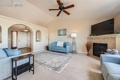 Carpeted living area with arched walkways, ceiling fan, lofted ceiling, and a tiled fireplace