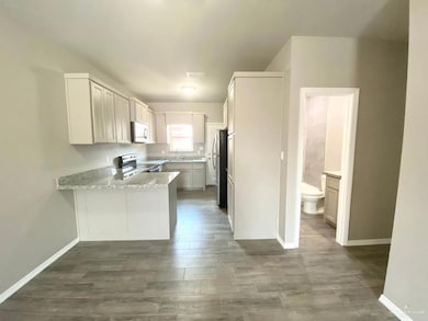 Kitchen with white microwave, range with electric stovetop, a peninsula, freestanding refrigerator, and wood finished floors