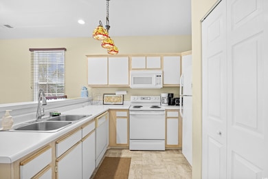 Kitchen with white appliances, light countertops, decorative light fixtures, and recessed lighting