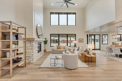 Living area featuring recessed lighting, a stone fireplace, light wood finished floors, a towering ceiling, and ceiling fan