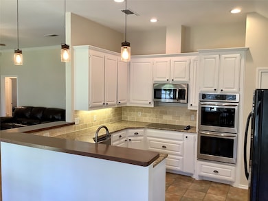 Kitchen featuring a peninsula, tasteful backsplash, black appliances, white cabinetry, and hanging light fixtures