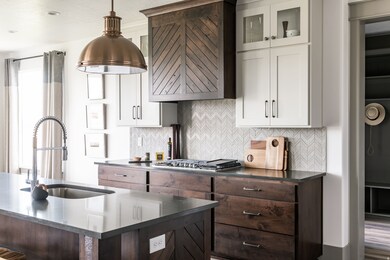 Kitchen with backsplash, dark brown cabinetry, white cabinets, decorative light fixtures, and glass insert cabinets