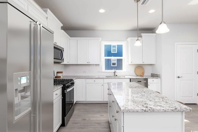 Kitchen with appliances with stainless steel finishes, light wood-style floors, white cabinets, a center island, and recessed lighting
