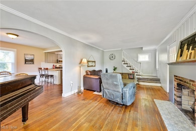 Living area with crown molding, arched walkways, light wood finished floors, a brick fireplace, and stairway