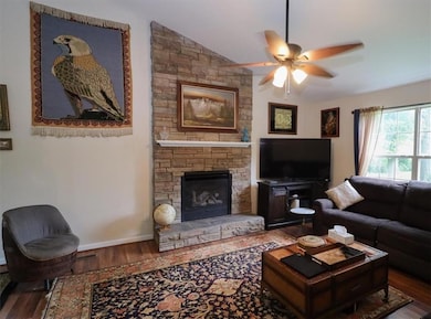 Living area with wood finished floors, a ceiling fan, a stone fireplace, and lofted ceiling