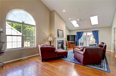 Living room featuring a fireplace, vaulted ceiling with skylight, a high ceiling, and light hardwood floors