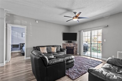Living room featuring baseboards, a textured ceiling, ceiling fan, a fireplace, and wood finished floors