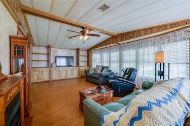 The expansive living room features vaulted ceilings with charming wood-look beams, built-in shelving, and large windows that flood the space with natural light.