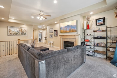 Living room with carpet, a fireplace, recessed lighting, a ceiling fan, and a tray ceiling