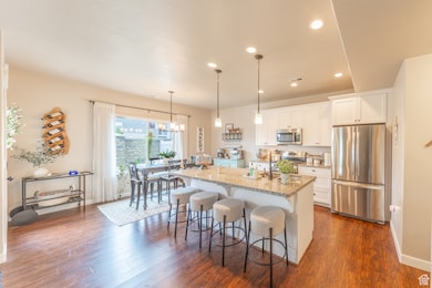 Kitchen with stainless steel appliances, light stone countertops, a breakfast bar, white cabinetry, and recessed lighting