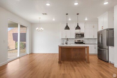 Kitchen with a center island with sink, decorative backsplash, appliances with stainless steel finishes, white cabinets, and hanging light fixtures