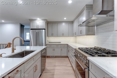 Kitchen with high end appliances, wall chimney range hood, light wood-style flooring, recessed lighting, and light stone counters
