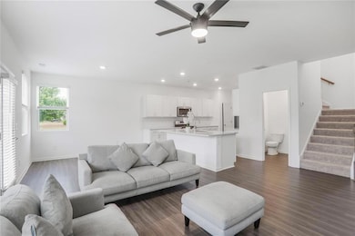 Living room with stairs, ceiling fan, dark wood-type flooring, baseboards, and recessed lighting