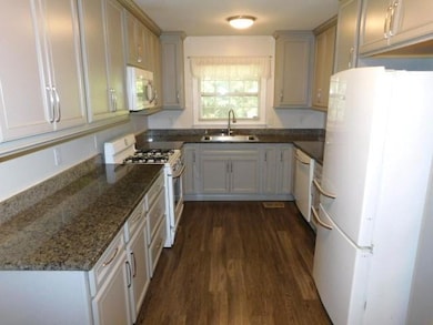 Kitchen featuring white appliances, dark wood-style floors, and dark stone countertops