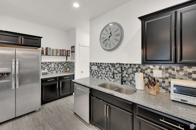Kitchen featuring appliances with stainless steel finishes, light stone counters, light wood-type flooring, tasteful backsplash, and recessed lighting
