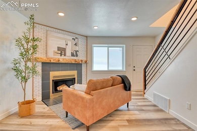 Living area featuring a tiled fireplace, baseboards, stairs, wood finished floors, and recessed lighting