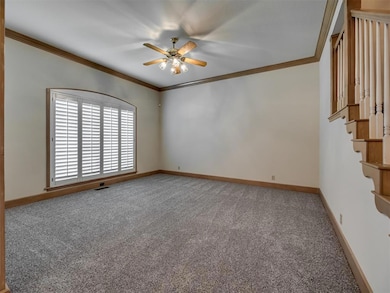 Carpeted empty room with ornamental molding, a ceiling fan, baseboards, and stairs