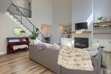 Living area featuring light wood-style floors, stairway, a glass covered fireplace, and a towering ceiling