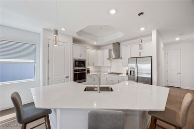 Kitchen featuring a breakfast bar, white cabinetry, stainless steel appliances, a tray ceiling, and decorative light fixtures