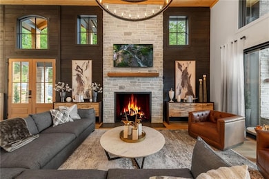 Living room featuring a 15ft ceiling, healthy amount of natural light, wood finished floors, a stone fireplace, and wooden walls