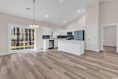 Kitchen featuring backsplash, high vaulted ceiling, decorative light fixtures, stainless steel appliances, and light countertops